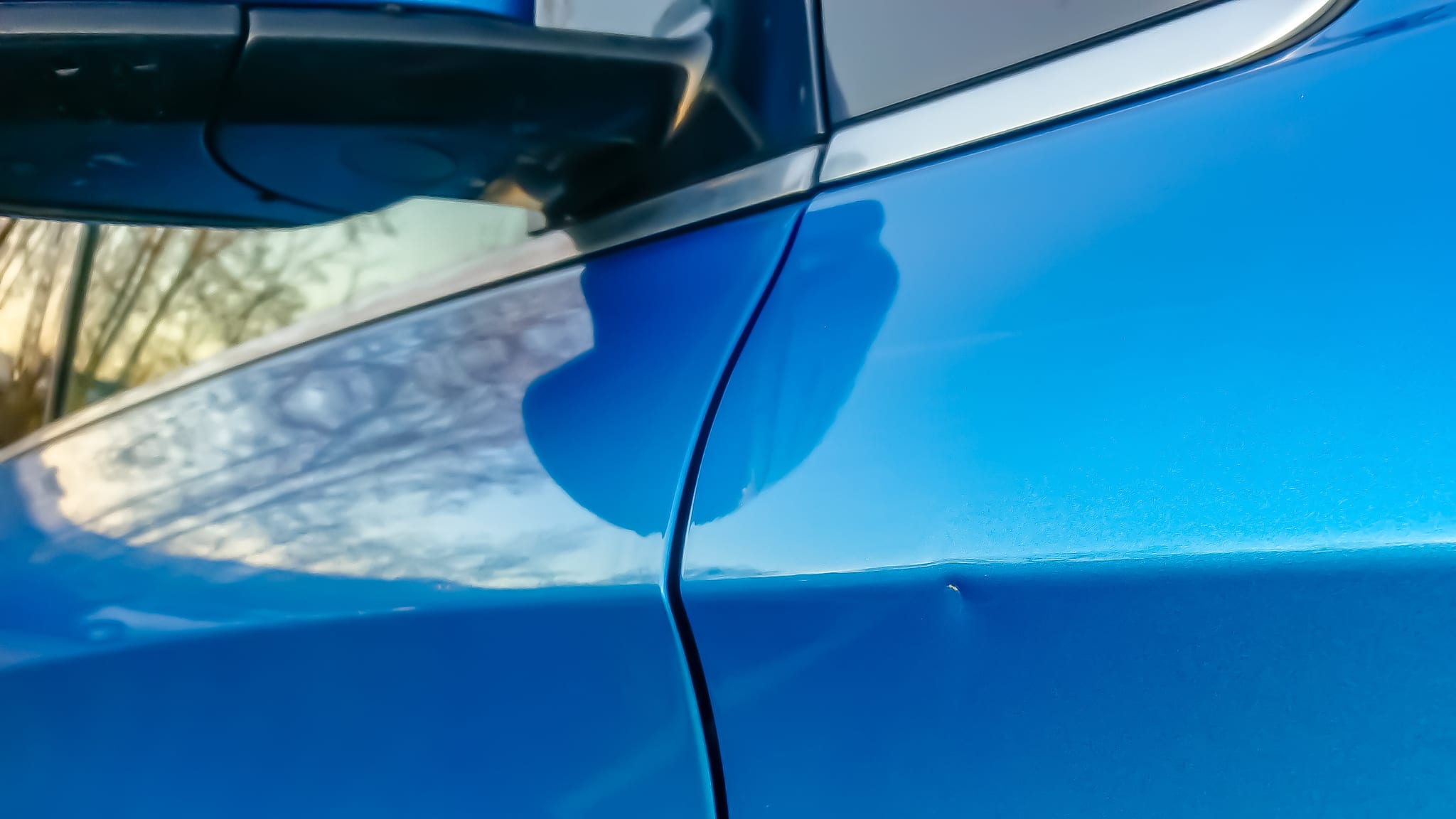 A small dent in the fender of a blue metallic car