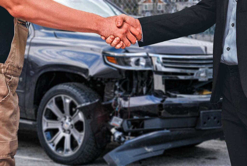 Mechanic And Professionally Dressed Customer Shake Hands In Front Of Damaged SUV