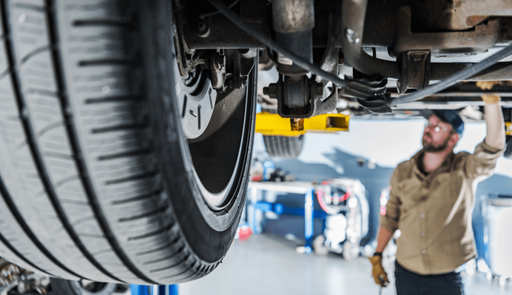 Auto body shop worker inspects suspension for hidden car damage.