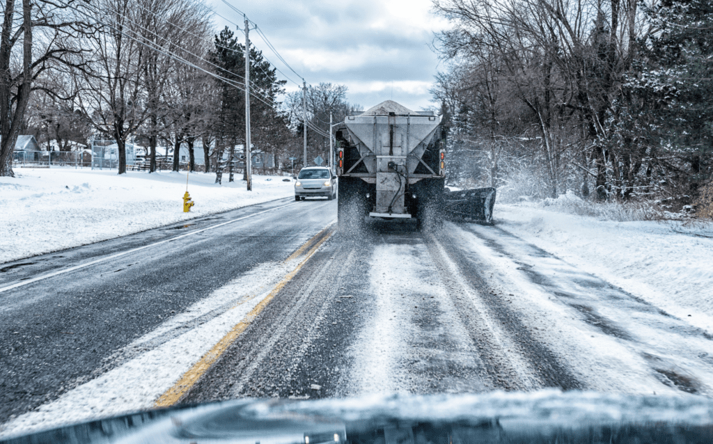 Truck spreading road salt as traffic drives on road.